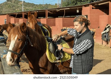 Man preparing horse for walk - putting on a saddle and bridle - Powered by Shutterstock