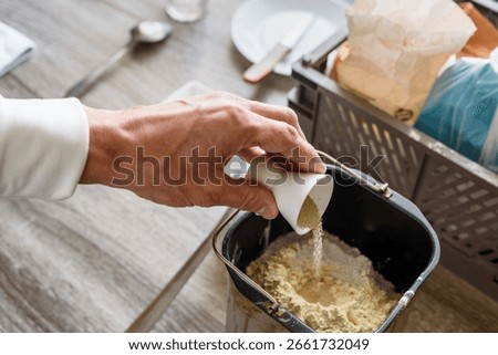 Man preparing ingredients for baking bread and adding yeast, closeup photo. Preparing dough for bread in a mold with flour, yeast, and bread maker, baking at home