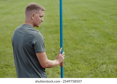 Man preparing for javelin throw while standing in open grassy field Holding javelin pole, appearing focused and ready for athletic performance Outdoors on a sunny day with green lawn in background