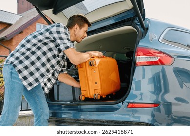 Man preparing for journey, loading suitcase in car trunk. Male traveler loading luggage for road trip