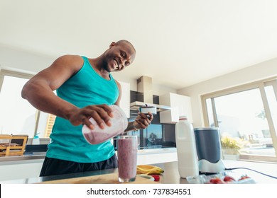 Man Preparing Milk Shake In Kitchen. Smiling Man Pouring Milkshake In A Glass For Drinking.