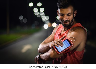 Man Preparing To Run Through The City At Night, He Tunes Music On The Phone.