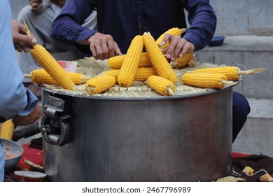 man preparing and selling boiled corn making it soft and ready to eat taking place in a market or street food setting where vendors prepare fresh hot food for customers
