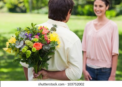 Man Preparing To Surprise His Friend By Giving Her A Bunch Of Flowers With Focus On The Man And The Flowers
