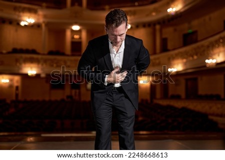 man Presenter in elegant classic suit on Stage is expressing gratitude to audience after performance, bow down, handsome american or european guy after successful presentation, skilled and talented
