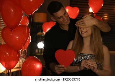 Man presenting gift to his girlfriend in room decorated with heart shaped balloons. Valentine's day celebration