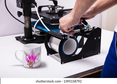 Man printing on coffee mugs in workshop