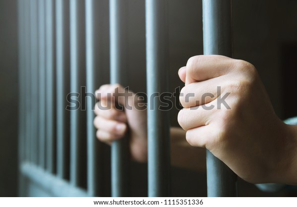 Man in prison hands of behind\
hold Steel cage jail bars. offender criminal locked in\
jail.