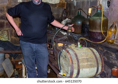 Man In The Private Wine Cellar Next To A Very Old Wine Barrels And A Large Bottle