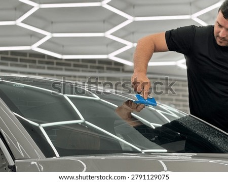 A man in the process of tinting the windshield. The concept of love for cars and protection. The process of installing the PPF on the windshield of a car. Athermal film on the windshield of the car. Car wrapping. Windshield protection. 