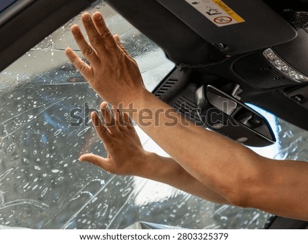 A man in the process of tinting the windshield. The concept of love for cars and protection. Athermal film on the windshield of the car. Car wrapping. Protection of the windshield from sunlight and heat.