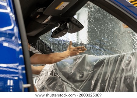 A man in the process of tinting the windshield. The concept of love for cars and protection. Athermal film on the windshield of the car. Car wrapping. Protection of the windshield from sunlight and heat.