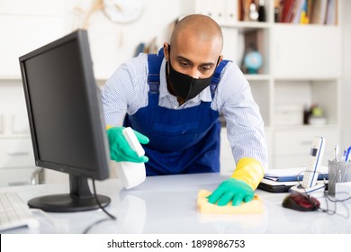 Man Professional Cleaner In Medical Mask Cleaning Desk With Computer In Office