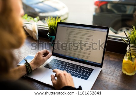 Man professional content writer working on web page via laptop computer while sitting in coffee shop during free time. Hipster boy smart developer sites using netbook for distance job