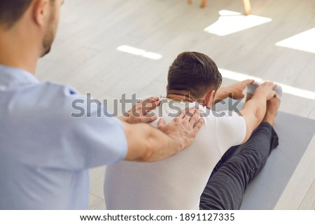 Man professional doctor osteopath fixing and stretching mans back with hands during exersicing on fitness mat at rehabilitation theapy in manual therapy clinic, top view. Chiropractor during work