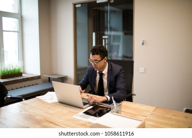 Man Professional Economist Searching Information In Internet On Laptop Computer While Sitting In Modern Office. Male Intelligent Employee Using Applications On Notebook During Work Day In Company 