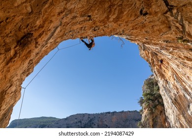 A Man Is Professionally Engaged In Extreme Sports, Mountaineering And Rock Climbing, Climbs The Ceiling, The Top Of The Cave Against The Blue Sky On A Sunny Day In Twin Caves, Arcadia, Greece.