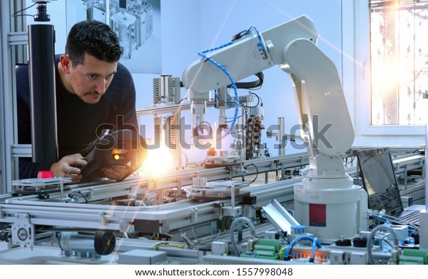Man is programming robotic arm with control panel\
which is integrated on smart factory production line. industry 4.0\
automation line which is equipped with sensors and robotic arm.\
Selective Focus.