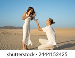 Man proposing to surprised woman on a sandy beach at dusk