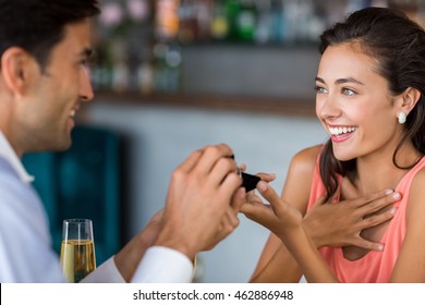 Man proposing to woman offering engagement ring in restaurant