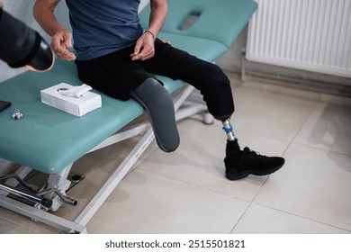 A man with a prosthetic leg sits on a medical examination table. The image conveys themes of resilience, healthcare, and rehabilitation. Tissue box placed nearby suggests personal care. - Powered by Shutterstock