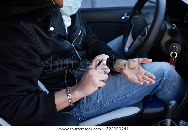 Man in protection mask sitting in the car,\
spraying hands antibacterial sanitizer spray for prevention\
coronavirus disease, health care\
concept.\
