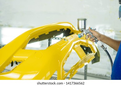Man with protective clothes and mask painting car using spray compressor ,yellow front bumper