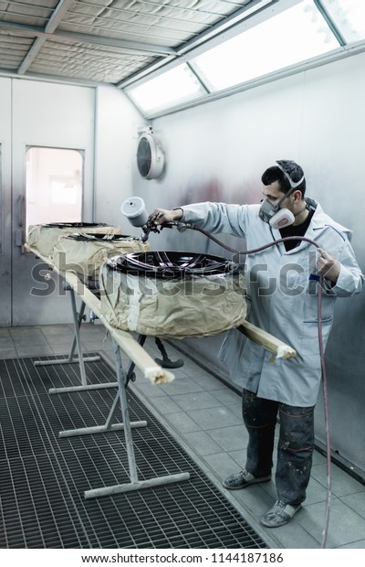Man with protective clothes\
and mask painting car parts using spray compressor. Selective\
focus. 