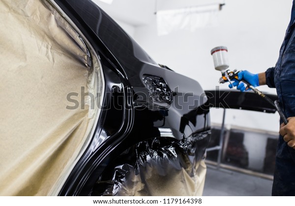 Man with protective clothes\
and mask painting car using spray compressor. Selective focus.\
