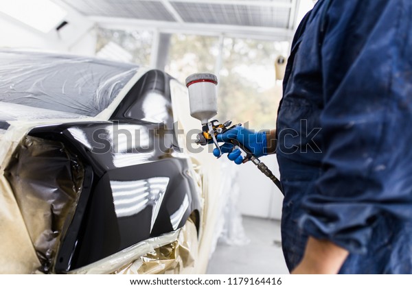 Man with protective clothes\
and mask painting car using spray compressor. Selective focus.\
