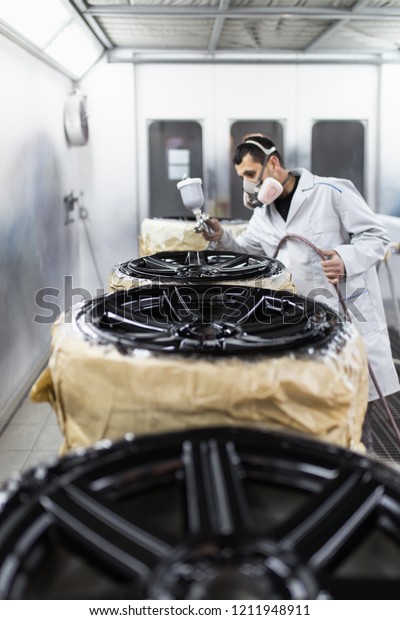 Man with protective clothes\
and mask painting car parts using spray compressor. Selective\
focus. 