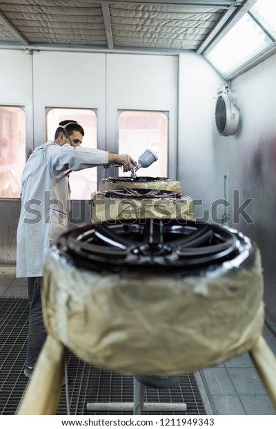 Man with protective clothes
and mask painting car parts using spray compressor. Selective
focus. 