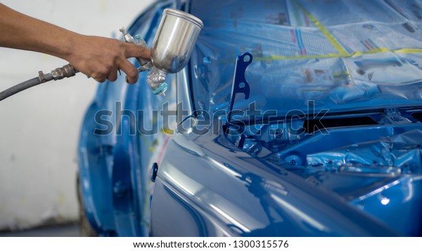 Man with protective clothes\
and mask painting car using spray compressor , Spay blue\
car
