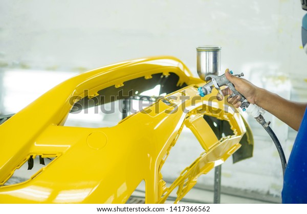 Man with protective\
clothes and mask painting car using spray compressor ,yellow front\
bumper