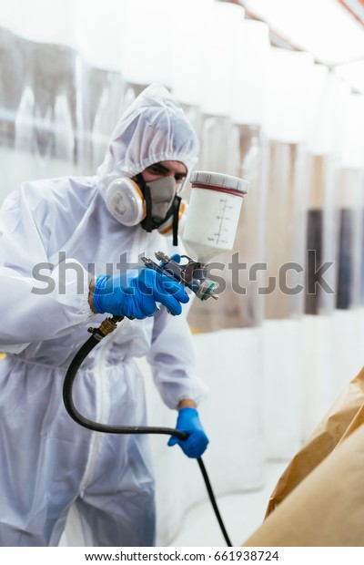 Man with protective\
clothes and mask painting car using spray compressor. Selective\
focus on hand. 