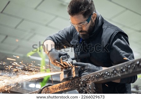 A man in protective clothing and glasses using a radial type grinder to cut a metal profile in the workshop. Young people find part-time work, Draftsman makes small businesses successful.