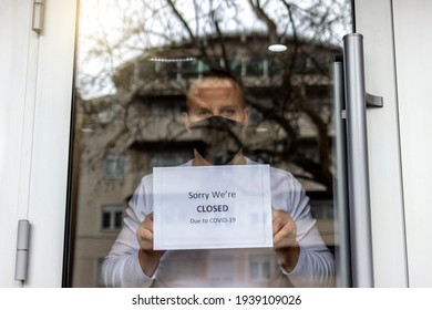 Man With Protective Face Mask Closing Business Activity Due To Covid-19 Emergency Lockdown Quarantine. Man With Protective Face Mask At Fitness Center Entrance Holding Closing Sign Due To Coronavirus.