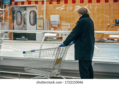 A Man In Protective Gloves And A Mask At Empty Shelves In A Supermarket.