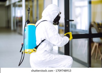 Man In Protective Hazmat Suit Washes Door Handles In Office To Preventing The Spread Of Coronavirus, Pandemic In Quarantine City. Cleaning And Disinfection Of Office. Covid-19.