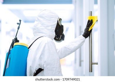 Man In Protective Hazmat Suit Washes Door Handles In Office To Preventing The Spread Of Coronavirus, Pandemic In Quarantine City. Cleaning And Disinfection Of Office. Covid-19.