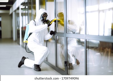 Man In Protective Hazmat Suit Washes Door Handles In Office To Preventing The Spread Of Coronavirus, Pandemic In Quarantine City. Cleaning And Disinfection Of Office. Covid-19.