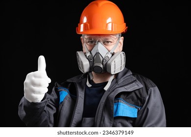 A man in a protective helmet, respirator and goggles shows a thumbs up on a black background. - Powered by Shutterstock