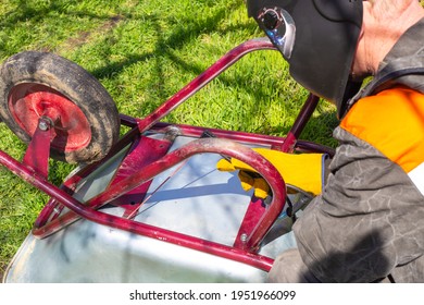 A Man In A Protective Helmet Welds A Metal Cart With An Electrode. Agricultural Machinery Repair.