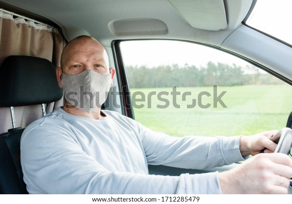 A
man in a protective mask driving a car. A man in a protective mask
driving a car goes to the pharmacy. A man in a gray sweater is
sitting in a car and wearing a mask from a
coronavirus.