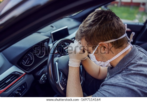Man with protective mask and gloves driving a car\
having headache. Infection prevention and control of epidemic.\
World pandemic. Stay safe.