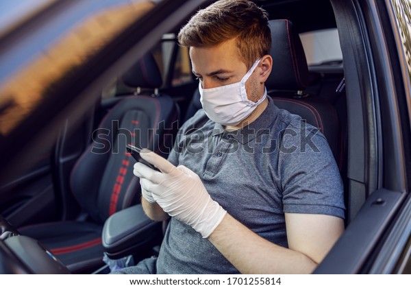 Man with protective mask and gloves\
driving a car holding mobile phone smartphone. Infection prevention\
and control of epidemic. World pandemic. Stay\
safe.