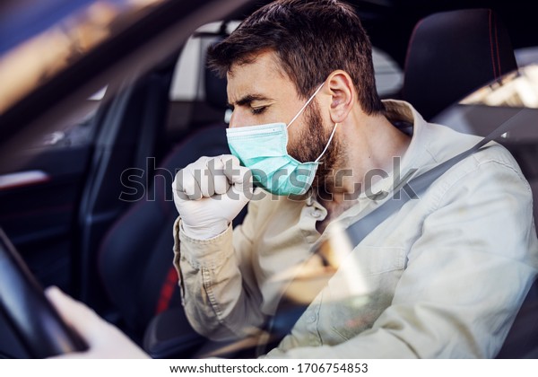 Man with protective mask and gloves driving a car\
coughing. Infection prevention and control of epidemic. World\
pandemic. Stay safe.