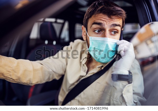 Man with protective mask and\
gloves driving a car talking on mobile phone smartphone. Infection\
prevention and control of epidemic. World pandemic. Stay\
safe.