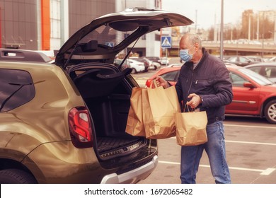 A Man With A Protective Mask On His Face Loads Food Packages Into The Car. Food Delivery. Coronavirus Covid-19