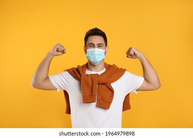 Man With Protective Mask Showing Muscles On Yellow Background. Strong Immunity Concept